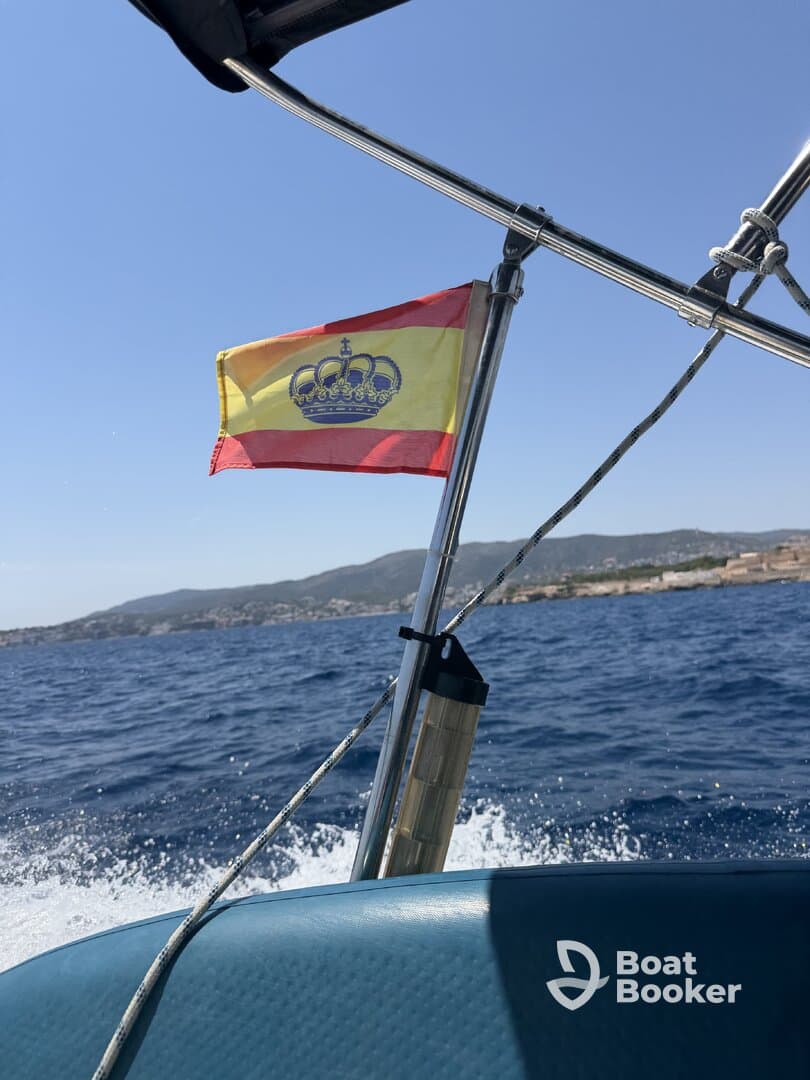 A vibrant Spanish flag flutters on a boat as it navigates through clear waters, showcasing a beautiful day on the sea.