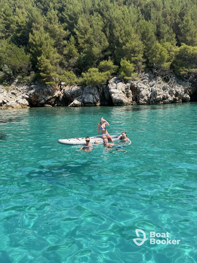 A joyful group enjoys a sunny day swimming and paddleboarding in crystal-clear waters, surrounded by lush greenery — a perfect summer getaway.