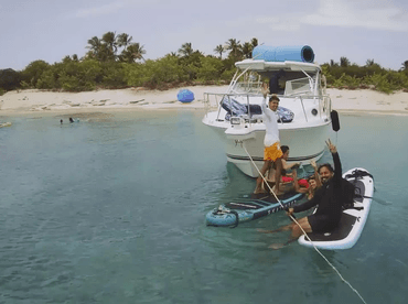 A lively group enjoys a fun day on the water, paddleboarding and swimming near a boat, creating unforgettable beach memories.