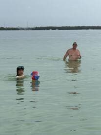 A family enjoys a fun day in the water, with a child playing with a beach ball and an adult nearby, capturing the essence of summer adventures.
