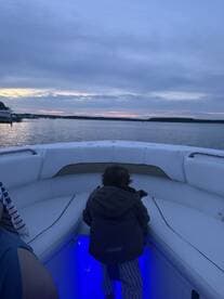 A child gazes out over the water from the deck of a boat during sunset, creating a serene family moment on the water.