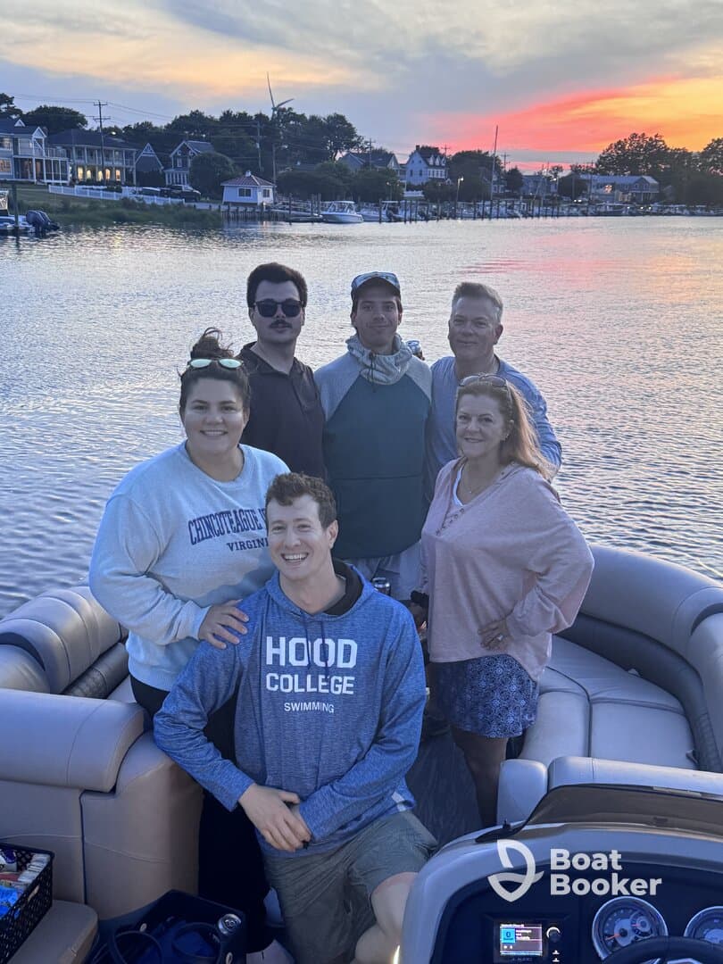 A cheerful group poses for a photo on a pontoon boat at sunset, capturing a memorable moment on the water — perfect for family gatherings or celebrations.