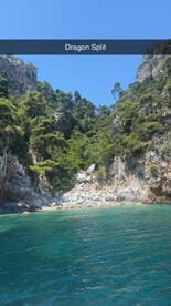 A stunning view of Dragon Split, showcasing lush greenery and rocky cliffs against crystal-clear waters — a perfect destination for boat tours and nature lovers.