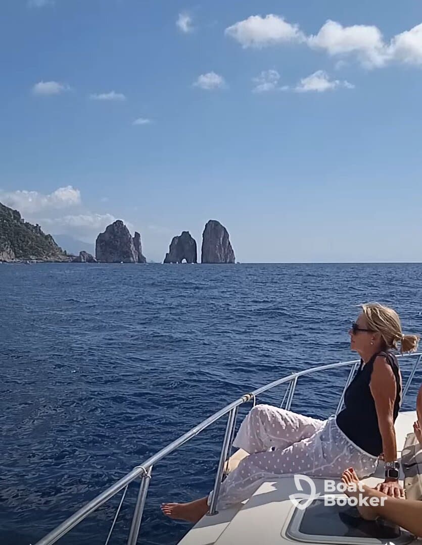 A woman relaxes on the bow of a boat, enjoying the stunning ocean view near the iconic rock formations of Capri — a perfect moment for leisure on the water.
