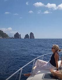 A woman relaxes on the bow of a boat, enjoying the stunning ocean view near the iconic rock formations of Capri — a perfect moment for leisure on the water.