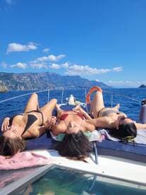 Three friends enjoy a sunny day on the boat, sunbathing and relaxing on the deck while surrounded by stunning ocean views.