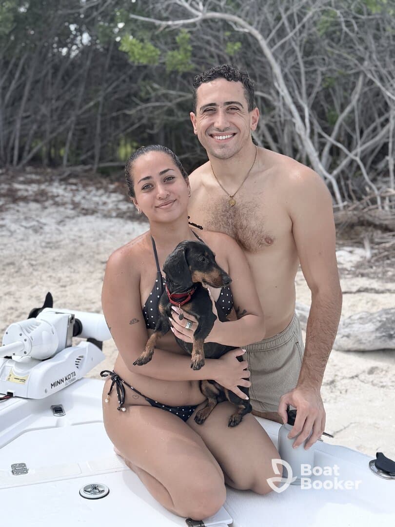 A happy couple poses with their dog on the deck of a boat, enjoying a sunny day at the beach — a perfect moment of fun and relaxation on the water.