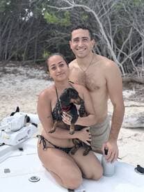A happy couple poses with their dog on the deck of a boat, enjoying a sunny day at the beach — a perfect moment of fun and relaxation on the water.