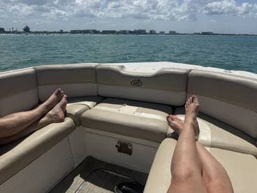 Relaxing on the lounge seating of a boat, with feet up and a scenic view of the water and shoreline — perfect for unwinding on a sunny day.