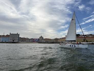 A sailboat glides through the waters of Lisbon, showcasing the vibrant cityscape in the background — a perfect scene for sailing enthusiasts and urban explorers alike.