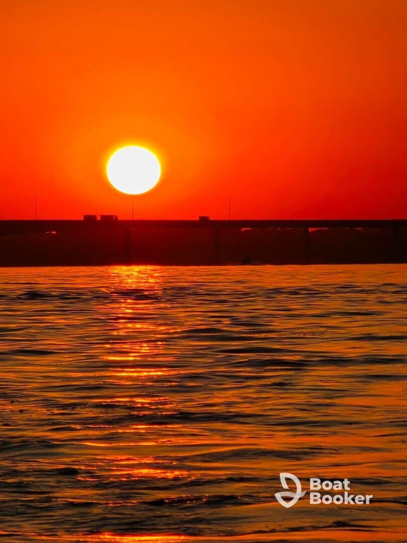 A breathtaking sunset casts vibrant orange hues over the water, creating a serene backdrop perfect for evening boat cruises.