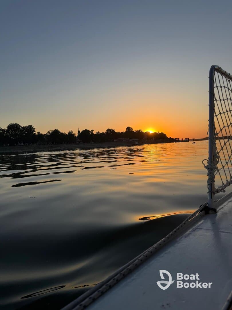 A serene sunset view from the side of a boat, showcasing tranquil waters and a picturesque shoreline — perfect for evening cruises.