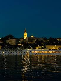 A beautifully illuminated boat glides along the river at night, reflecting the vibrant cityscape and creating a picturesque scene perfect for evening cruises.