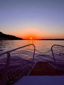 A stunning sunset view from the bow of a boat, showcasing tranquil waters and a vibrant sky — perfect for evening cruises.