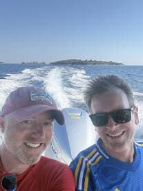 Two friends enjoy a sunny day on the water, capturing a selfie with a beautiful island backdrop — perfect for memorable boating adventures.