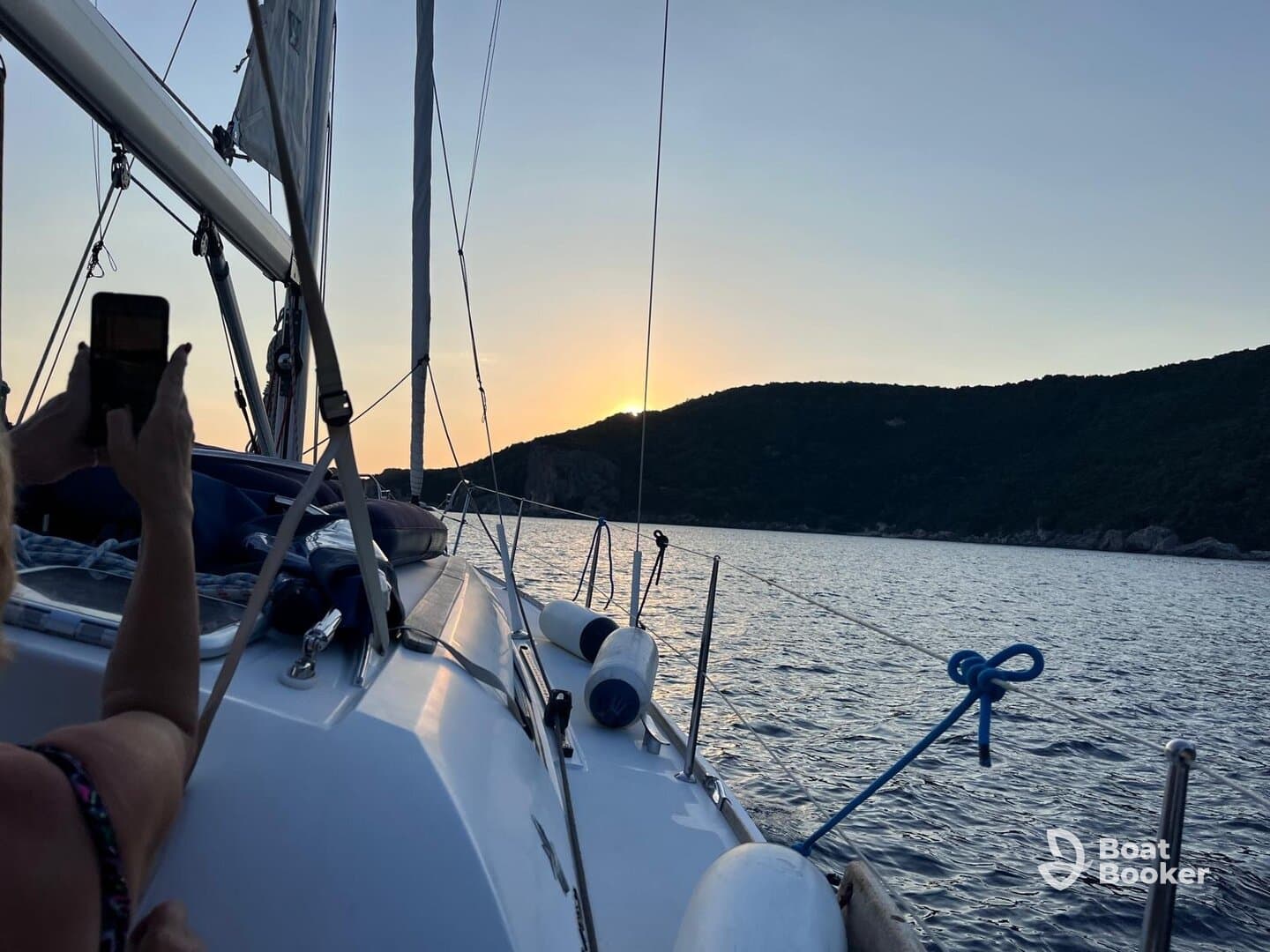 A beautiful sunset view from a sailboat, capturing a guest taking a photo while enjoying the serene waters and scenic landscape.