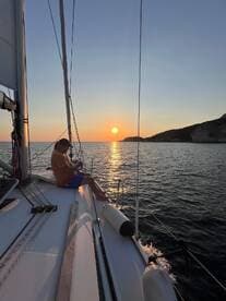 A serene moment as a person enjoys the sunset while sailing, capturing the essence of relaxation on the water.