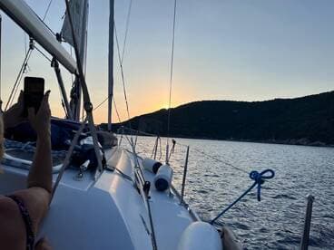 A beautiful sunset view from a sailboat, capturing a guest taking a photo while enjoying the serene waters and scenic landscape.