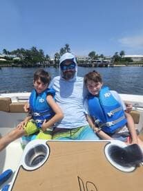 A father enjoys a sunny day on the boat with his two sons, all wearing life jackets, capturing a perfect family moment on the water.