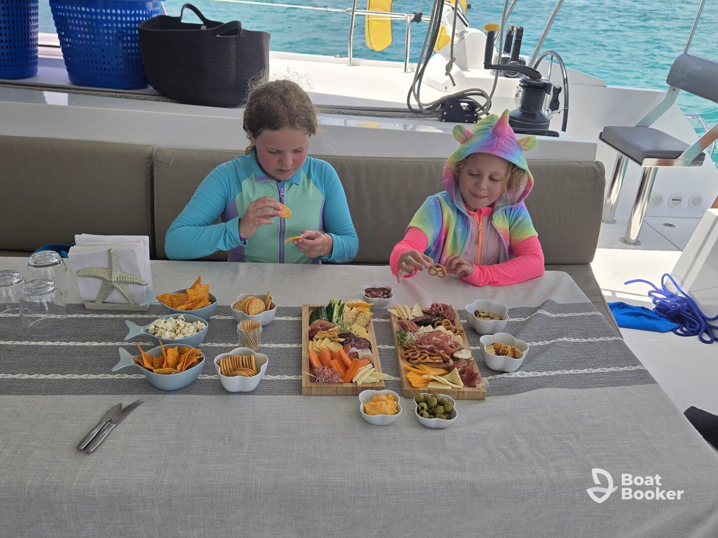 Two children enjoy a colorful spread of snacks and charcuterie aboard a boat, perfect for family outings and fun on the water.