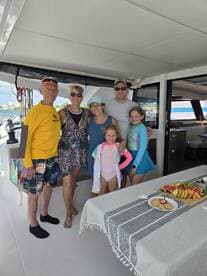 A joyful family poses together inside a boat, showcasing a delightful spread of fruits and snacks — perfect for memorable gatherings on the water.