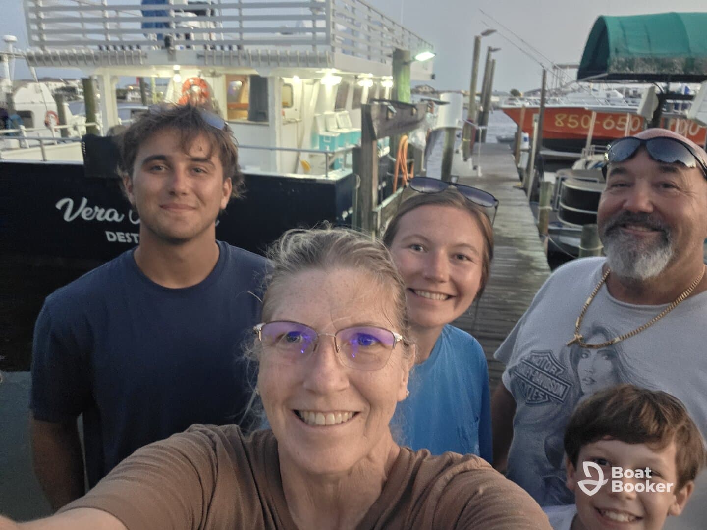 A cheerful family takes a selfie in front of the 'Vera C' boat at the dock, capturing a memorable moment together before their adventure.