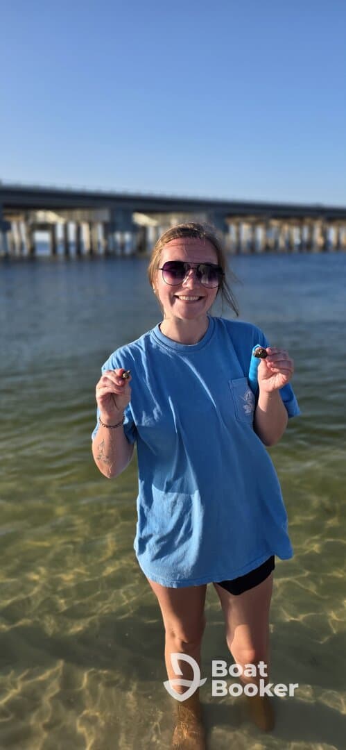 A joyful moment captured as a woman stands in shallow water, showcasing her catch while enjoying a sunny day by the pier — perfect for memorable beach outings.