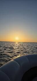 A serene sunset view from the edge of a boat, capturing the tranquil waters and the golden horizon — perfect for evening cruises.