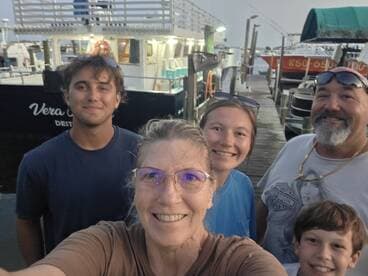 A cheerful family takes a selfie in front of the 'Vera C' boat at the dock, capturing a memorable moment together before their adventure.