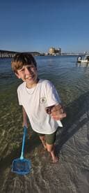 A young boy proudly holds a shell while wading in shallow waters, showcasing a fun and adventurous day by the beach.