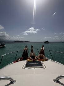 A group of friends relaxes on the bow of a boat, soaking up the sun and enjoying the beautiful turquoise waters — perfect for a day of leisure on the water.