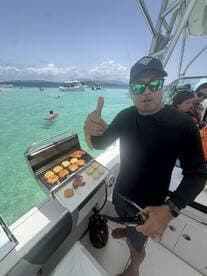 A chef prepares a delicious barbecue on a boat grill, showcasing a variety of meats and buns — perfect for a fun day on the water.