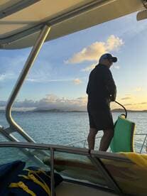 A man stands on the deck of a boat during sunset, preparing for an enjoyable evening on the water. The scenic backdrop enhances the boating experience.