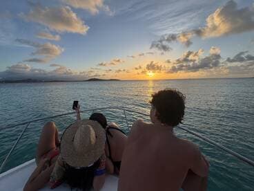 A group enjoys a stunning sunset aboard a boat, capturing the moment with a phone — perfect for memorable evenings on the water.