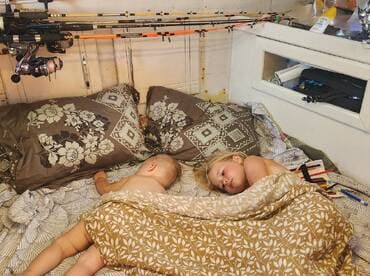 Two young children peacefully sleeping in a cozy cabin aboard a boat, surrounded by fishing gear and comfortable bedding.