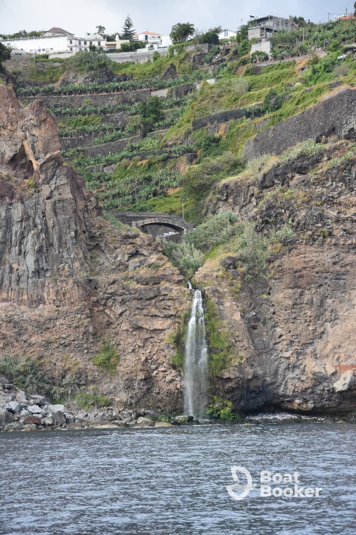 A stunning waterfall cascades down rocky cliffs, surrounded by lush greenery, showcasing the natural beauty of the coastline.