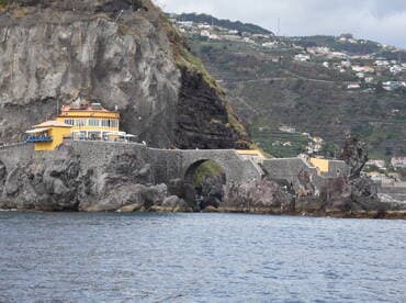 A scenic view of a coastal area featuring a vibrant yellow building and people enjoying the rocky shoreline — a perfect destination for beachgoers and nature lovers.