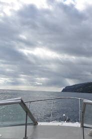 A serene view from the bow of a boat, showcasing the expansive ocean and distant coastline under a cloudy sky — perfect for exploring coastal waters.