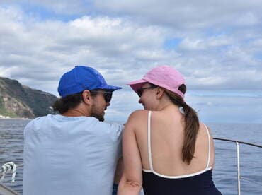 A couple enjoys a romantic moment on a boat, gazing at the ocean and mountains in the background — perfect for memorable getaways.