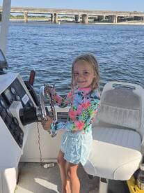 A young girl joyfully steers a boat, showcasing the excitement of learning to navigate on the water — a perfect moment for family boating adventures.