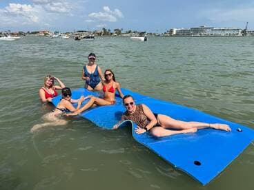 A lively group of friends enjoys a fun day on the water, lounging on a floating mat while soaking up the sun — perfect for summer adventures.