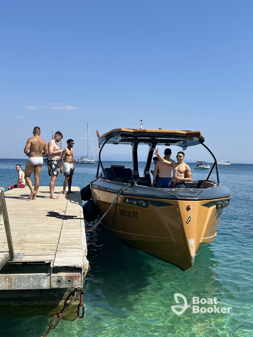 A lively group enjoys a sunny day by the water, with a stylish boat docked nearby — perfect for beach parties and summer fun.