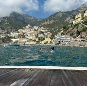 A couple enjoys a refreshing swim in the clear waters off the picturesque Amalfi Coast, with colorful hillside buildings creating a stunning backdrop.