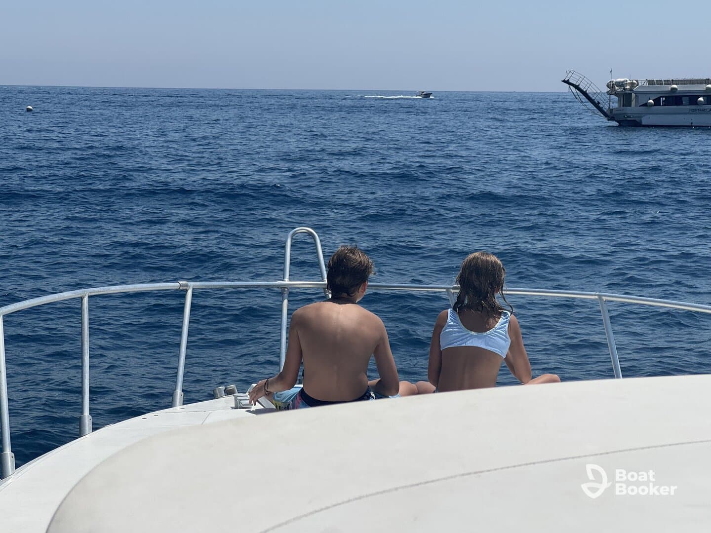 Two children enjoy the serene ocean view from the bow of a boat, capturing a perfect moment of relaxation on the water.