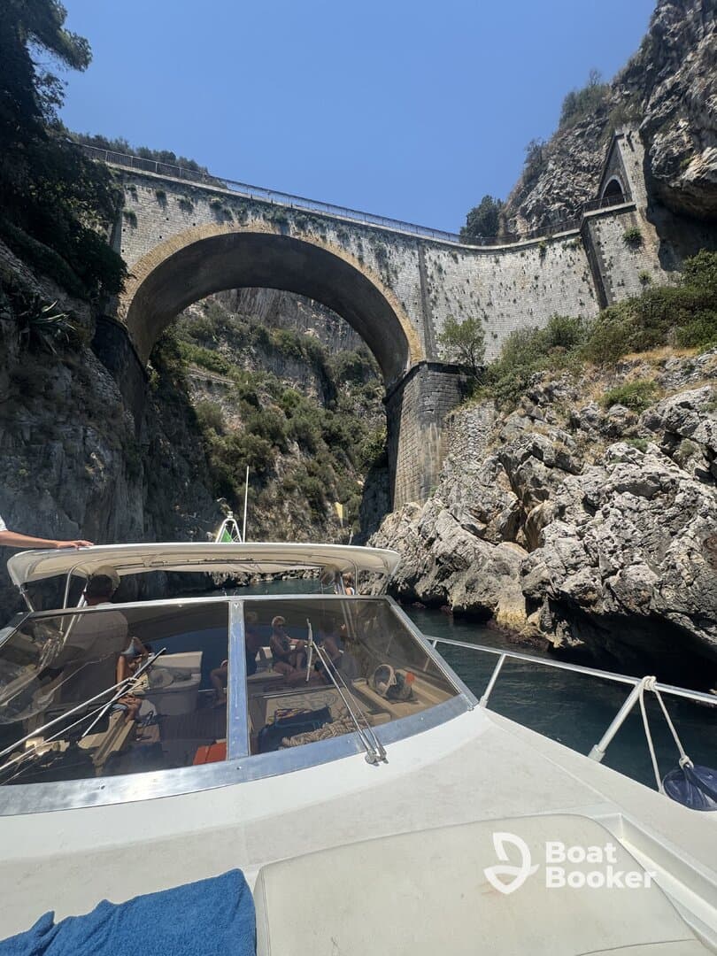 A scenic view of a boat navigating through a rocky gorge beneath a historic bridge, showcasing the stunning coastal landscape — perfect for adventure seekers exploring hidden gems.
