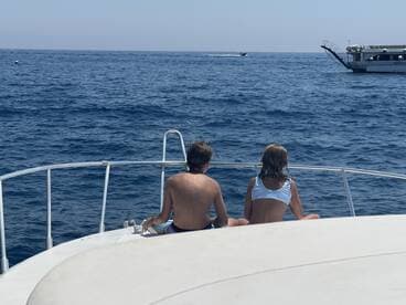 Two children enjoy the serene ocean view from the bow of a boat, capturing a perfect moment of relaxation on the water.