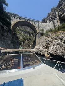 A scenic view of a boat navigating through a rocky gorge beneath a historic bridge, showcasing the stunning coastal landscape — perfect for adventure seekers exploring hidden gems.