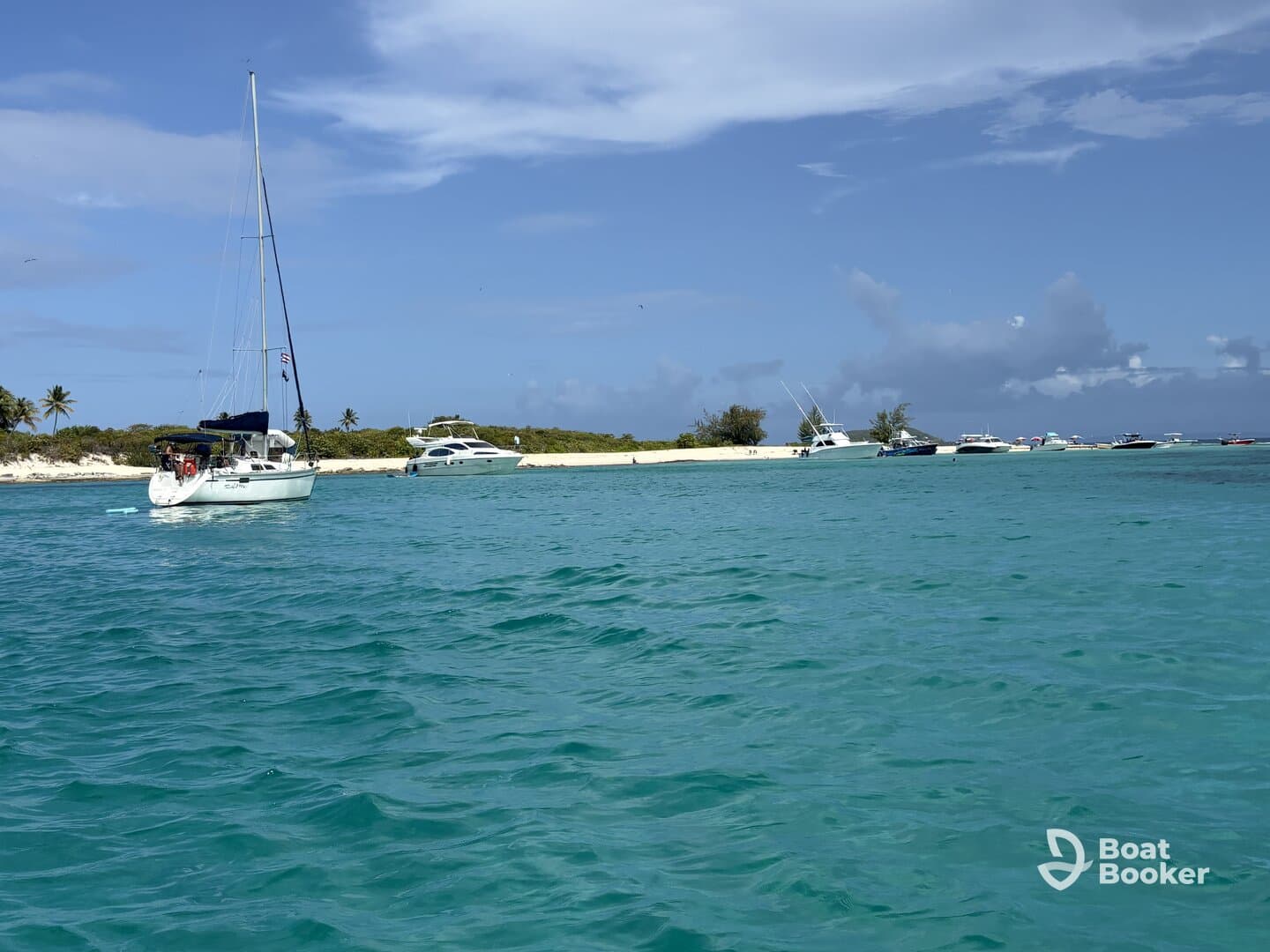 A picturesque view of a sailboat navigating through clear turquoise waters, surrounded by other vessels and a sandy shoreline, perfect for showcasing boating adventures.