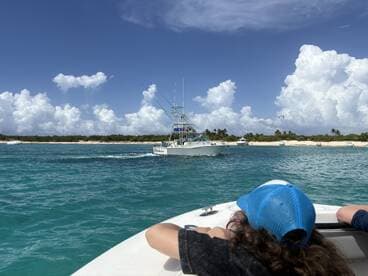A scenic view of a fishing boat cruising through turquoise waters, with a beach in the background and a child enjoying the ride — perfect for family adventures on the water.