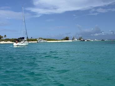 A picturesque view of a sailboat navigating through clear turquoise waters, surrounded by other vessels and a sandy shoreline, perfect for showcasing boating adventures.